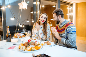 Young couple having festive dinner sitting together in the modern house during the winter holidays