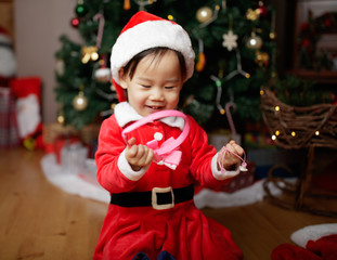 toddler baby girl wearing santa claus costume play in front of christmas tree