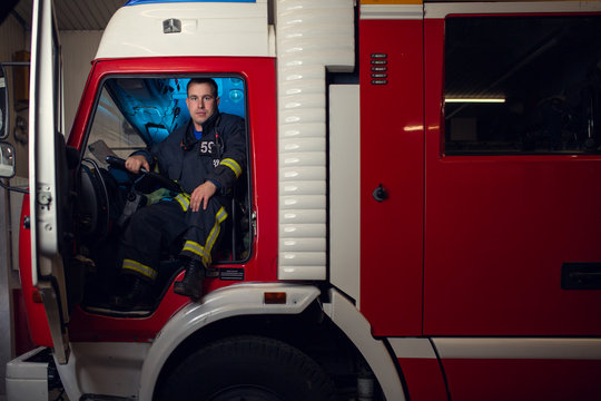 Image of young fireman man sitting in fire truck