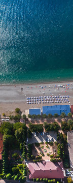 hotel is surrounded by green trees on the turquoise sea, beach with umbrellas. top down view.