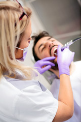High angle view of a beautiful young female dentist polishing or repairing dental cavity on male patient's teeth. Health care and medicine concept