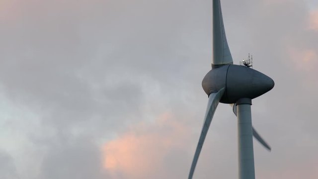Wind turbine with turning blades in the wind in an offshore windpark during sunset.