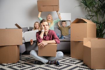 Photo of upset man sitting on floor and women with boy and girl sitting on gray sofa