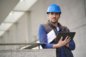 Handsome building expert in hardhat outdoors with tablet and blueprint