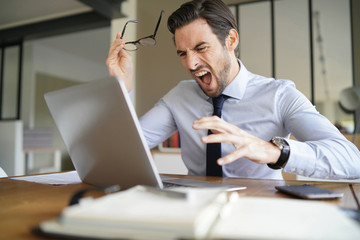 Fototapeta premium Angry businessman losing patience and screaming at laptop in modern office