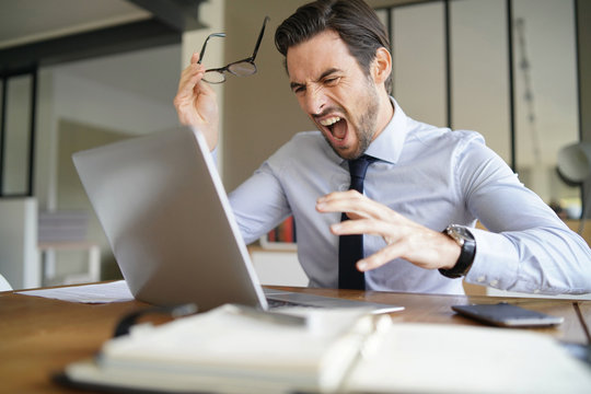 Angry Businessman Losing Patience And Screaming At Laptop In Modern Office