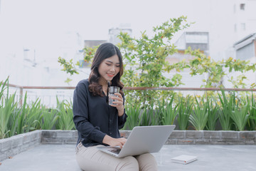 Enjoying nice time on fresh air. Beautiful young woman working on her laptop and smiling while sitting in floor on her outdoor house terrace