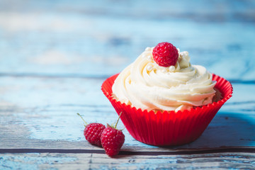 Vanilla cupcakes with cream and raspberries on a blue wooden background. Birthday muffins for a colorful party.