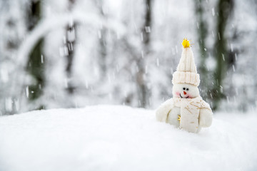 A smiling snowman in a hat and scarf in a snowdrift under falling snow.