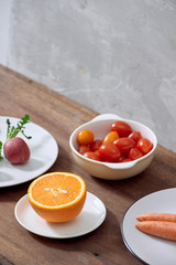 variety of ingredients in a dish, isolated on gray orange, carrot, radish and plum tomato