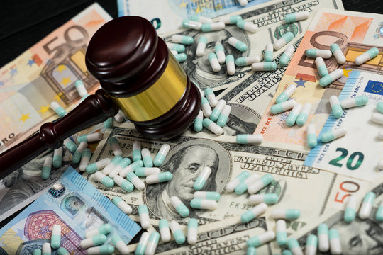Wood judge's gavel and scattered colorful drugs on the dollar and euro cash background