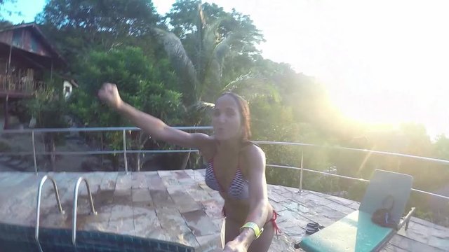 Young attractive brunette woman in bikini jumps into swimming pool on tropical resort during beautiful sunset. Slow Motion. 1920x1080.