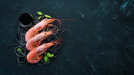 Black pasta with shrimp on a black stone background. Top view. Free space for your text.