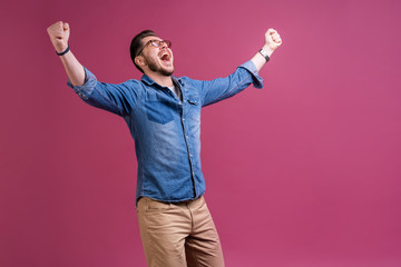 Portrait of a satisfied young man celebrating success isolated over pink background.