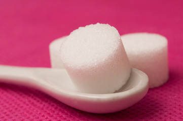  closeup of sugar in shaped circle in white spoon on pink background