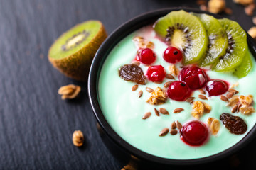 Healthy food colorful Yogurt Breakfast Bowl  with kiwi, flax seeds, Granola, and red currants in black ceramic bowl with copy space