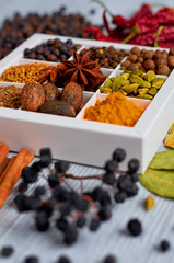 Indian spices and herbs in the box on the gray table: anise stars, fragrant pepper, cinnamon, nutmeg, bay leaves, paprika - ingredients for tasty food and cuisine. Spices texture background. Side view