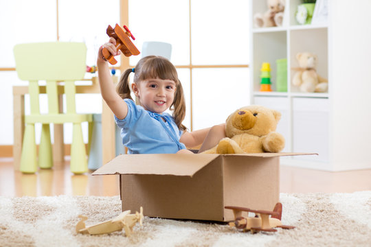 Happy little girl plays pilot sitting into cardboard box in flat