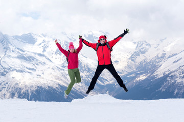 white man and woman in winter clothes on the background of snowy mountains, people jump