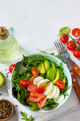 Diet menu, Vegan food. Healthy salad with arugula, Tomatoes, Salmon, Egg and Avocado on a white stone table. Copy space.