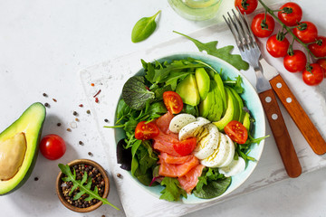 Diet menu, Vegan food. Healthy salad with arugula, Tomatoes, Salmon, Egg and Avocado on a white stone table. Top view flat lay background. Copy space.