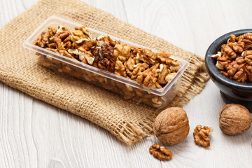 Walnuts in plastic container and stone bowl on a wooden background.