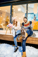 Young happy couple dressed in sweaters celebrating winter holidays with bengal fire in front of a beautiful decorated house