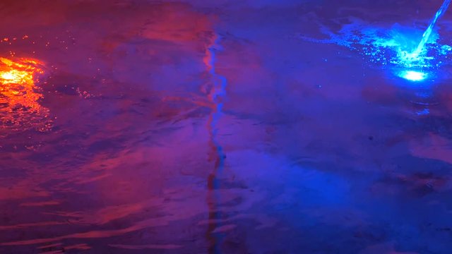 Glowing color underwater lights in the fountain. Blue and red lamps under water. Beautiful evening illumination. Water texture.
