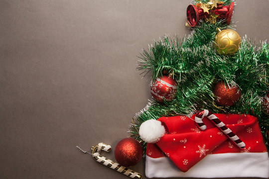 Christmas tree of green garland with Santa's hat and red balls on a gray background