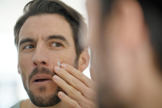 Handsome Man Applying Face Cream Looking In Mirror