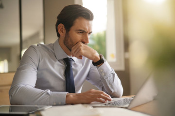 Handsome businessman working hard on laptop in modern office