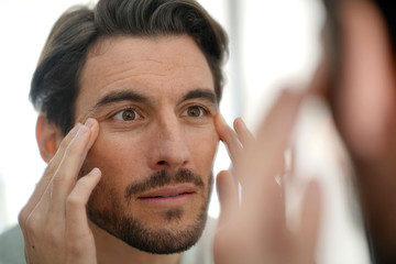 Handsome man checking wrinkles in mirror at home - obrazy, fototapety, plakaty