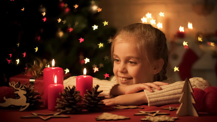 Adorable child looking at candles and wooden toys on table, Christmas decoration