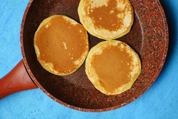 Ruddy pancake in a pan on a blue background. Close-up. View from above.