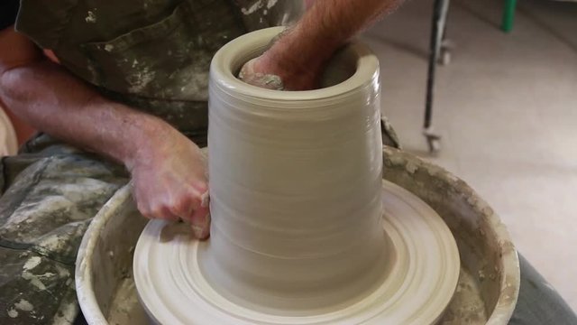 Artist potter in the workshop creating a ceramic vase. Hands closeup. Twisted potter's wheel. Small artistic craftsmen business concept.