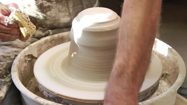 Artist potter in the workshop creating a ceramic vase. Hands closeup. Twisted potter's wheel. Small artistic craftsmen business concept. 