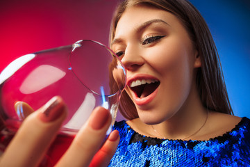 The surprised young woman in party clothes posing with glass of wine. Emotional female cute face. View from the glass