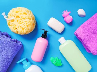 Purple towel, yellow sponge, pink package liquid soap, green shampoo bottle and rubber toys for kids. Flat lay baby bath products