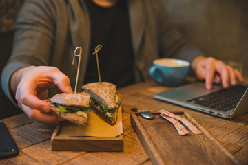 Obraz premium man taking sandwich in cafe. working with laptop. close up. no faces