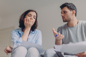 Photo of serious female and male do paperwork together, review bank documents and hold pen, discuss something, look thoughtfully, speak about something, think about future plans, sign contract
