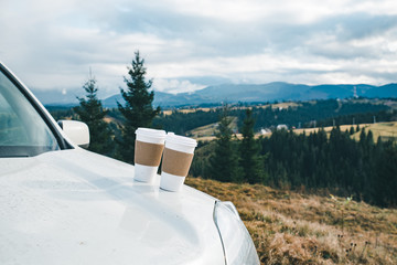 car close up with two coffee cups on the hood mountains on background