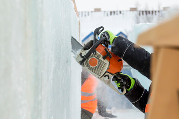 Worker cuts a lump of ice with a chainsaw