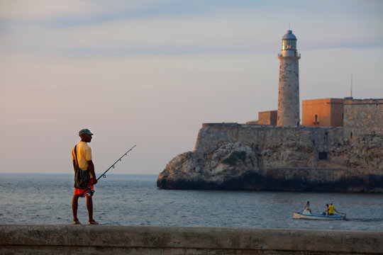 A fisherman standing on the railing on the Malecon at the entrance to the harbor in Havana, Cuba.