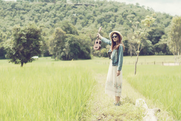 Young woman in a field , rounded sunglasses and straw hat and ukulele having fun outdoor in countryside.Awesome warm summer day.