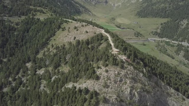 Aerial footage of Rock Del Quer at the green Pyrenean mountains in the summer. Drone flies over the Rock Del Quer, between green mountains of Andorra La Vella, Andorra. There are winding roads in the