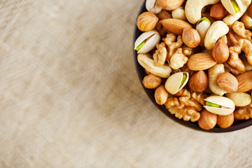 Mix of various nuts in a wooden cup against the background of fabric from burlap. Nuts as structure and background, macro. Top view.