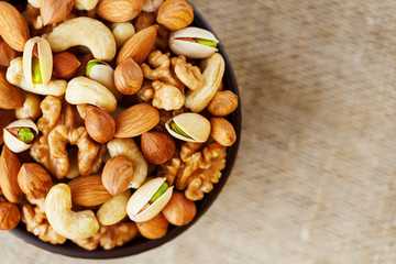 Mix of various nuts in a wooden cup against the background of fabric from burlap. Nuts as structure and background, macro. Top view.
