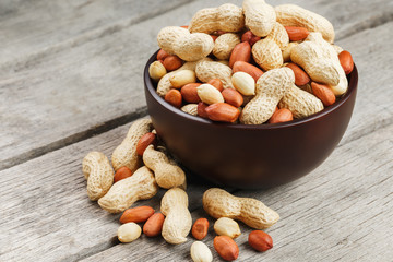 Roasted peanuts in the shell and peeled in a cup, against a gray wooden table