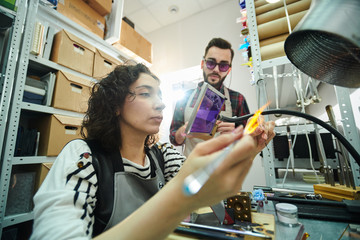 Low angle portrait of young woman shaping glass over gas torch while making beads for beautiful handmade jewelry in glassworking studio, copy space