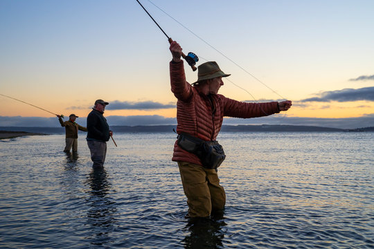 Two fly fishermen cast for searun coastal cutthroat trout and salmon with their guide standing between them on a salt water beach on a beach on the west coast of the USA
